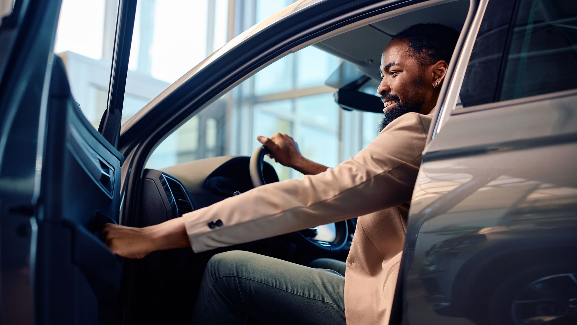 Happy African American man getting inside of his new car after buying them in showroom.